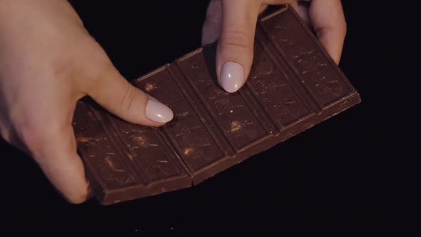 Woman Breaks Black Chocolate Bar with Nuts