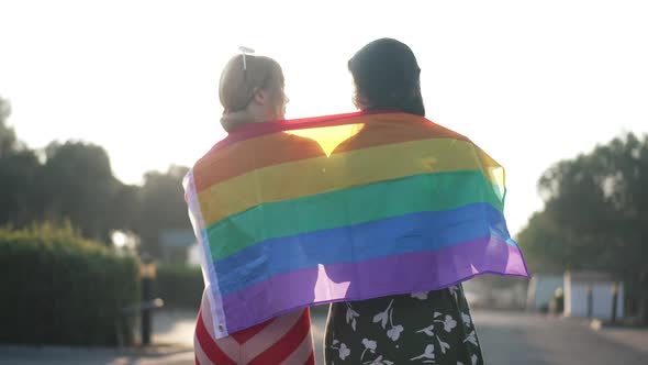Happy Smiling Caucasian Lesbian Couple Walking in Sunrays with Rainbow Flag Talking