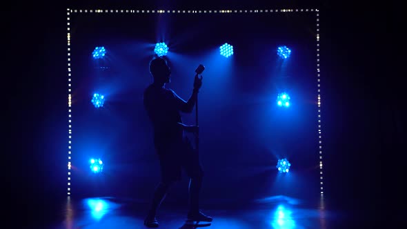 A Male Singer Performs in a Dark Studio with Dynamic Blue Lights. The Guy Is Expressively Singing