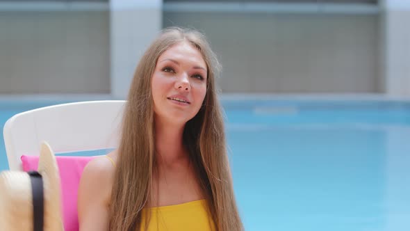 Beautiful European Blonde Girl Sitting By Summer Pool on Hot Day Fanning Herself Waving Straw Hat