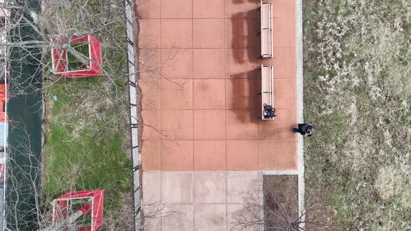 a top down shot directly over a paved walkway with benches and dry trees in a park. The drone camera