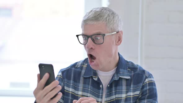 Portrait of Casual Middle Aged Man Celebrating Success on Smartphone 