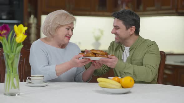 Grateful Adult Son Hugging Senior Mother Smiling Talking Thanking for Delicious Baked Dessert