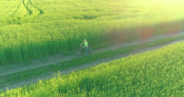 Aerial View on Young Boy, That Rides a Bicycle Thru a Wheat Grass Field on the Old Rural Road