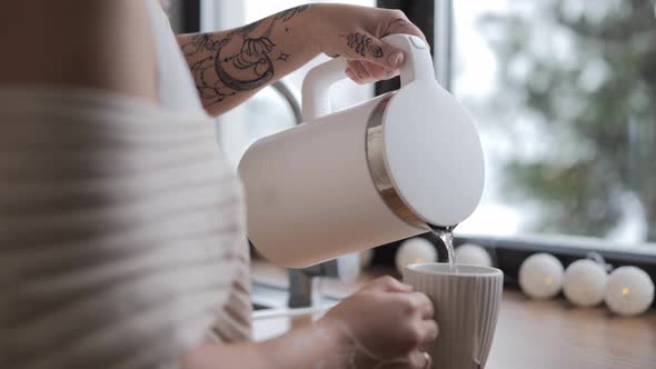 Woman Hand Pours Hot Tea of Kettle Into Cup at Home