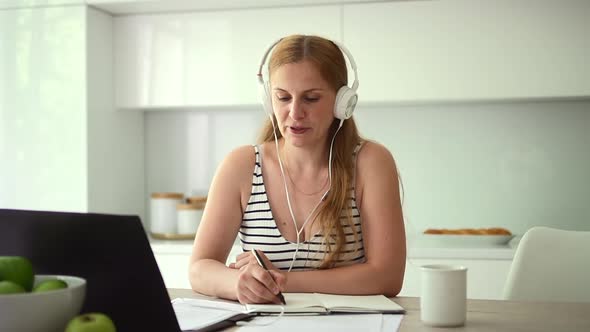 Woman Writing and Listening While Self Study at Table with Laptop in Home Room Spbd