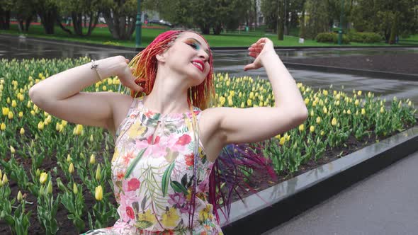 A Girl with Bright Makeup and African Rainbow Braids is Enjoying the Arrival of Spring in Blooming