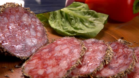 The Knife Cut a Delicious Dry Sausage in Herbs on a Wooden Board Into Slices