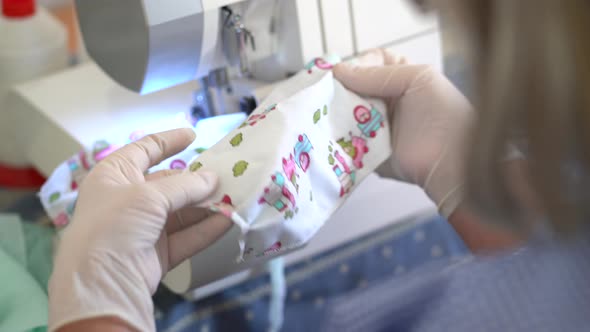 Female artisan on protective gloves sewing fabric masks