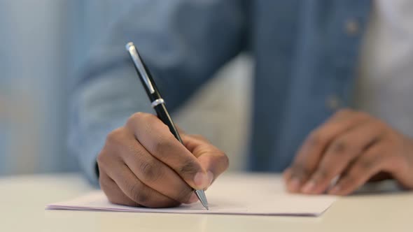 Hands of African Man Writing on Paper with Pen Close Up