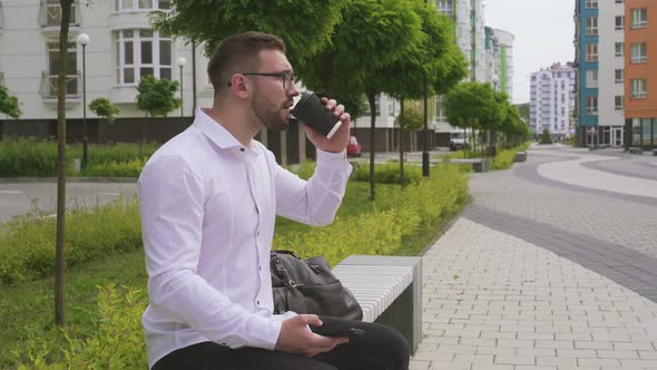 Man Using Smartphone and Drinking Coffee Outdoors