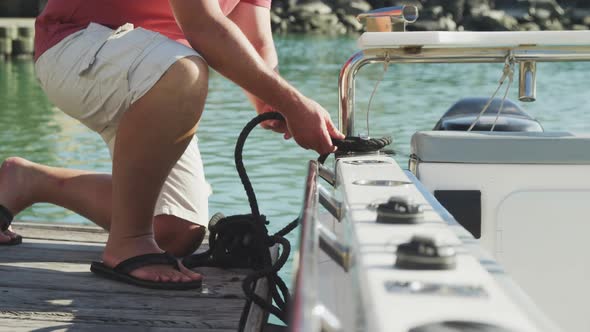 Side view low section of a Caucasian man untying a rope on the boat harbor side