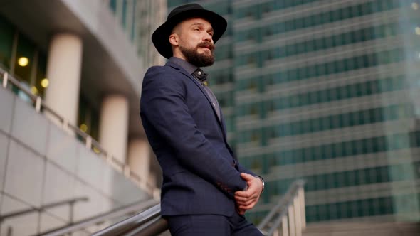 Stylish Mustache Man in Luxury Suit and Hat is Standing Alone in Modern Business District