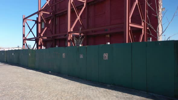 A low angle shot of an old building's red facade behind a green wooden fence. The camera boom up to