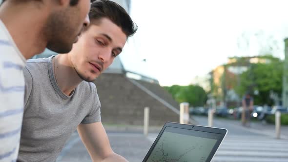 two young multiethnic men sitting outdoor using digital tablet and personal computer