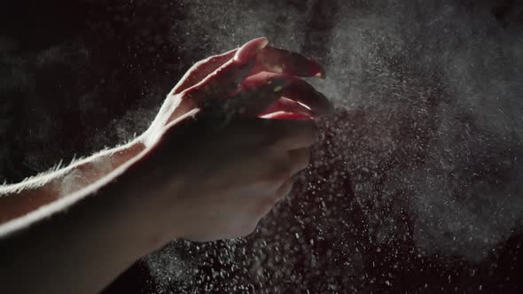 A Woman Claps Her Hands with Talcum Powder on a Dark Background