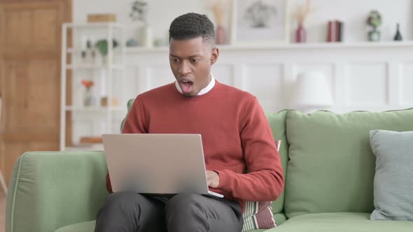 African Man with Laptop Feeling Shocked on Sofa