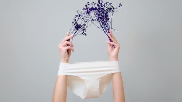 Female's hands, which hold dry violet plants, arms are wearing white panties