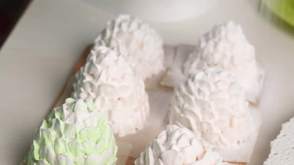 A Woman Sprinkles Powdered Sugar On Marshmallow Cones. Marshmallow Cones Of White And Light Gree