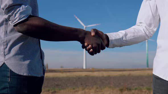 Two Male African American Electrical Engineers Stand Against the Backdrop of a Windmill at an Air