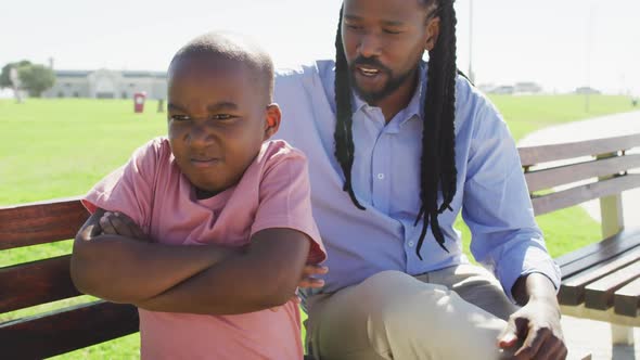 Video of african american father sitting on bench and talking with angry son