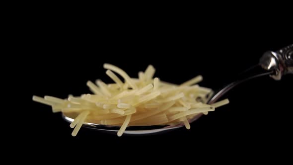 A full metal spoon of thin small uncooked vermicelli. Falling raw pasta