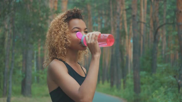 Black Woman Drinking From Pink Bottle. Portrait of Black Young Woman Taking Break While Jogging
