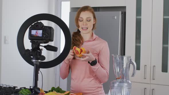 Woman holding a bowl of chopped fruit and recording it with digital camera in the kitchen