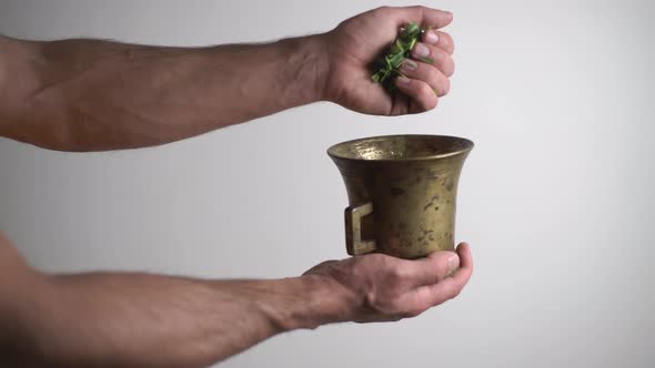 A Man Adds Medicinal Herbs Tarragon to a Copper Bowl Prepares a Cough Tincture White Background