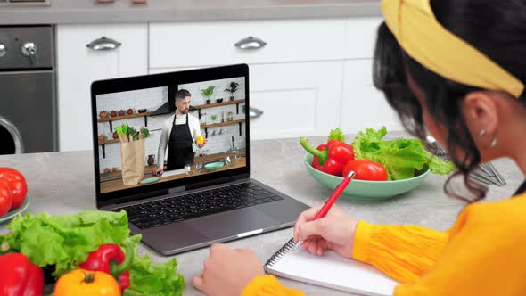 Woman in Kitchen Watch Online Cooking Course Listen Chef Writes in Notebook