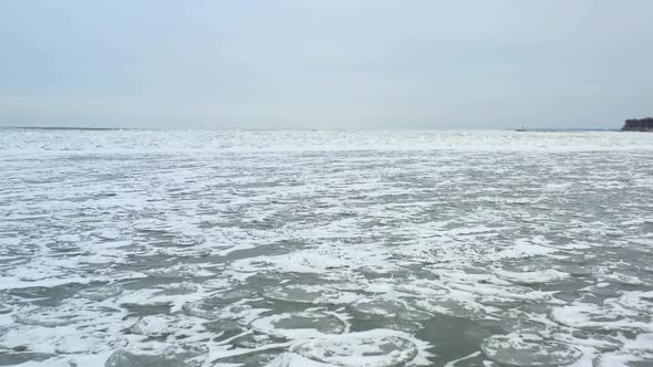 Drone flying over frozen water. Flying forward and slow on a cold windy day. Snow covered textured i