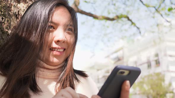 Close up of Asian woman with black straight hair and happy face. Standing and using her smart phone