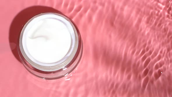 White Facial Cream on Pink Background with Water Ripples and Splashes on Surface