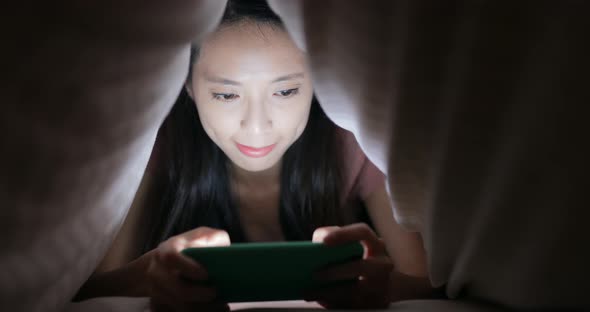 Woman using cellphone under blanket at night