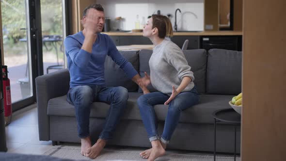 Wide Shot Angry Couple Shouting Gesturing Sitting on Couch in Living Room at Home