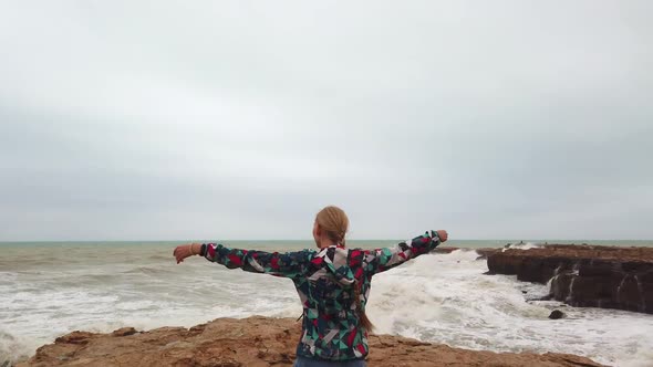 Girl Raises Her Hands Up While Standing with Her Back on the Seashore During a Storm