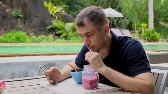Young Man Read Social Media News Feed in Smartphone Drink Fruit Shake in Cafe