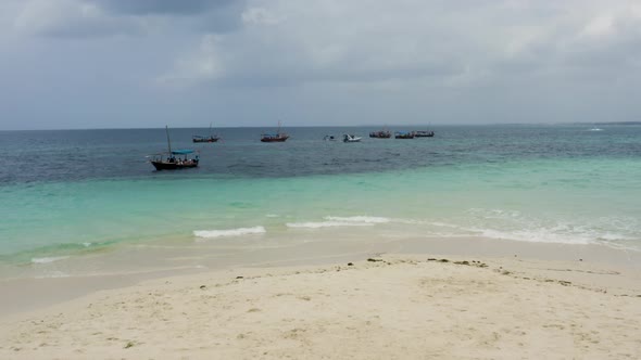 Boats anchored just offshore white sand beach in Zanzibar, one sailing.