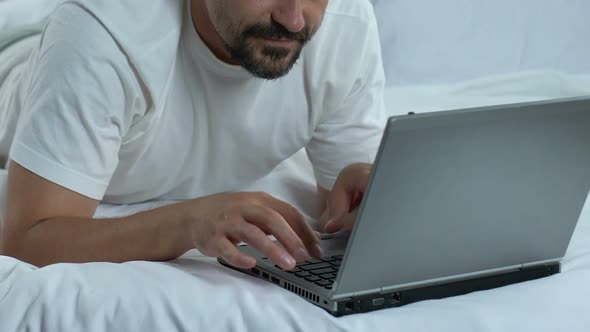 Man Typing Laptop Lying in Bed and Showing Thumbs Up, Freelancer Working Online