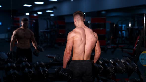 Handsome young athlete working out on a mirror background. Young man lifting dumbbells. 