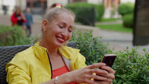 Portrait of a Laughing Blonde in Red and Yellow Clothes with a Phone in Hands Against the Background