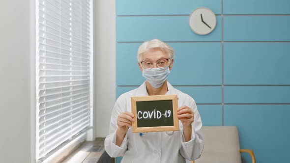 Senior woman doctor with disposable mask holds blackboard