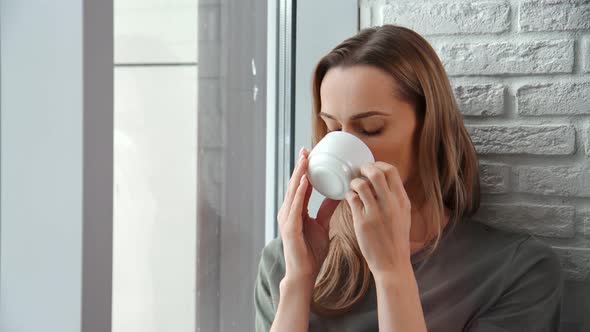 Contemplative Domestic Young Woman Drinking Coffee Looking Through Window Enjoying Loneliness