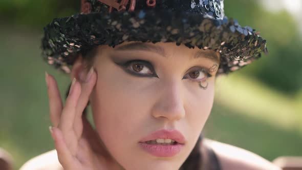 Headshot Young Slim Beautiful Woman in Steampunk Hat with Extravagant Makeup Looking at Camera As in