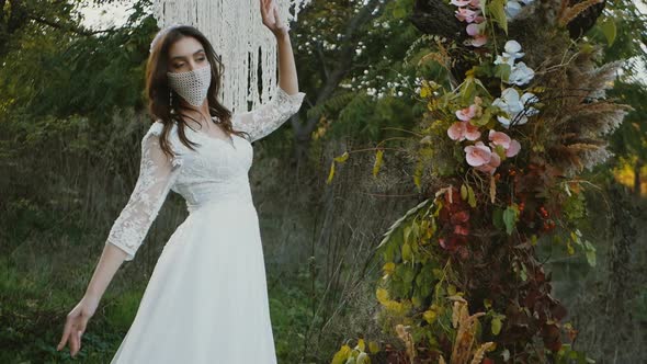 portrait of a bride in a mask posing. Beautiful young bride in a wedding dress in the park. On her f