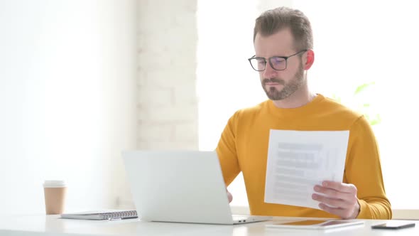 Man with Laptop Reading Documents in Office