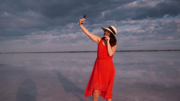 Young Woman Takes a Selfie in a Beautiful Unusual Place. Girl in a Red Dress, Hat and Sunglasses on