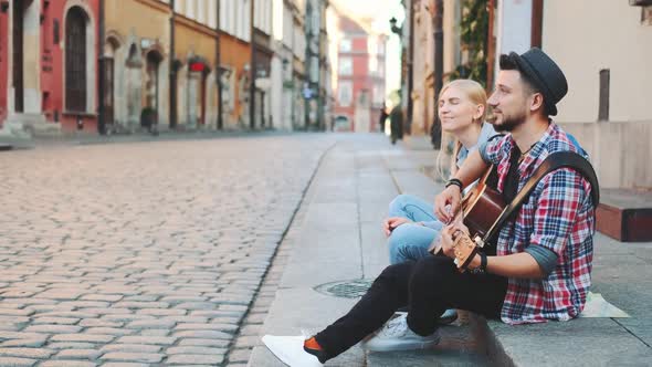 Tourists Sitting on Sidewalk Playing Guitar and Having Rest