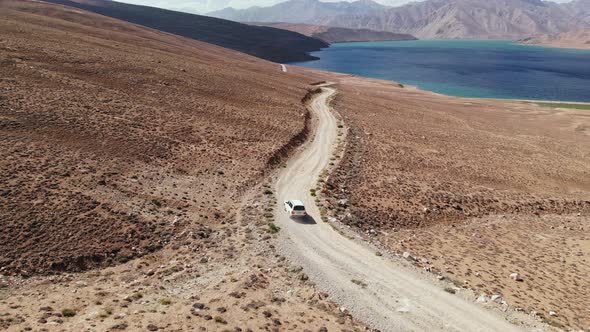 Aerial Over Off Road 4X4 Car Driving Along Gravel Trail Path Toward Lake in Arid Mountains