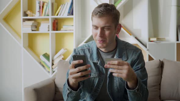 Online Payment. Man Holding Debit Card and Using Smartphone for Shopping at Home